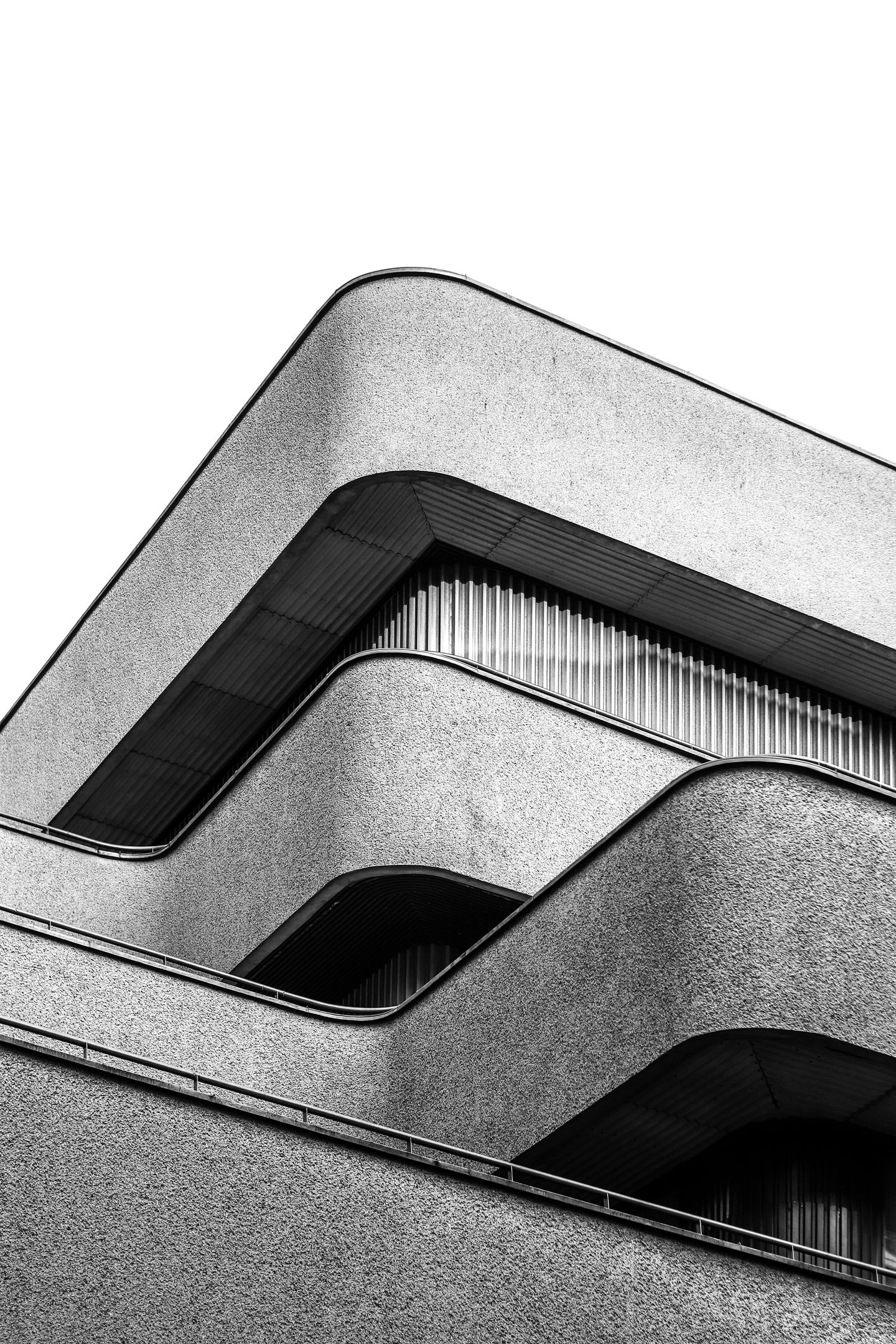 Geschwungene Betonfassade mit Bändern vor grauem Himmel